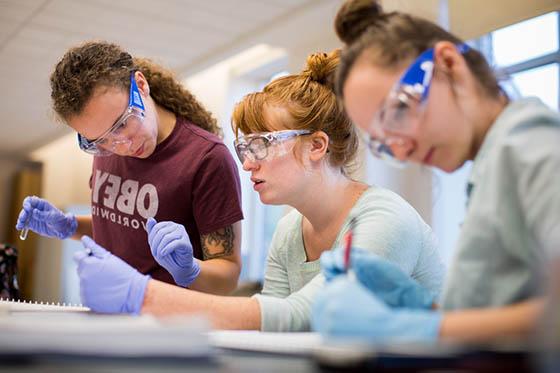 图为三名立博体育官网的女学生戴着护目镜和手套在实验室工作